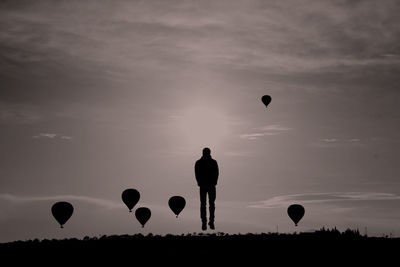 Silhouette person levitating by hot air balloons flying against sky during sunset