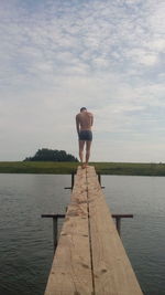 Rear view of man standing on pier over lake against sky