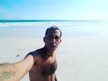 Portrait of shirtless young man at beach against sky