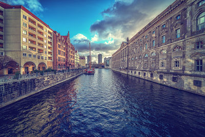 Canal amidst buildings in city against sky