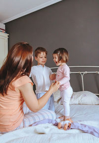 Cheerful mother playing with son and daughter on bed at home