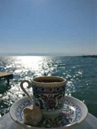 Close-up of coffee on table by sea against clear sky