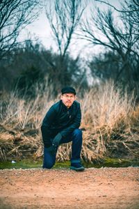 Portrait of man kneeling against bare trees