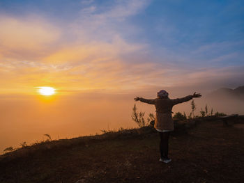 Rear view of woman standing on field against sky during sunset
