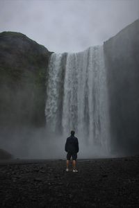 Rear view of man looking at waterfall falling from mountain