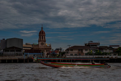 Boats in canal by buildings against sky in city