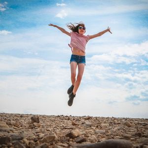 Low angle view of woman jumping against sky