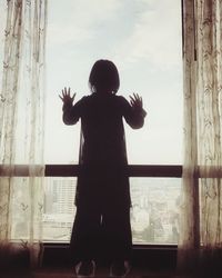 Silhouette boy playing with window against sky