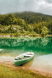 Morning on the lake in bavarian alps. green boat near coast, clouds in mountains, germany.
