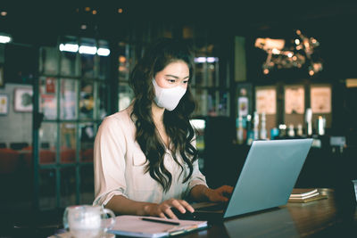 Businesswoman wearing mask using laptop at home