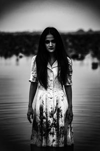 Portrait of young woman standing against lake