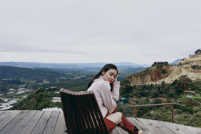 Portrait of young woman sitting on railing against mountain