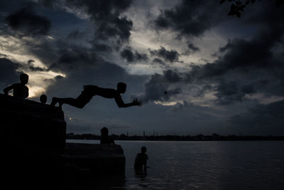 Silhouette people standing by sea against sky during sunset