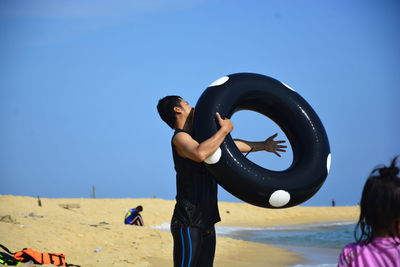 Man holding inflatable ring on beach against sky