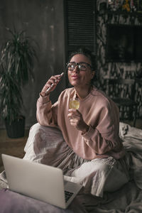 Young woman using phone while sitting on laptop