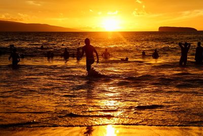 Silhouette people on beach against sky during sunset