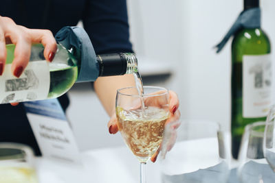 Midsection of person pouring wine in glass on table