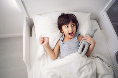 Child boy lies in a white children's bed with a blanket in a room with toys rabbits