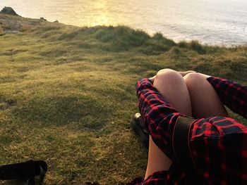 Low section of woman sitting on field by sea