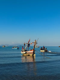 Fishing boats in sea against clear blue sky