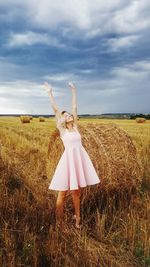 Happy woman standing with arms raised on field against sky