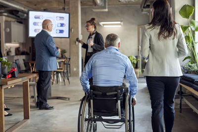 Rear view of businessman with disability by businesswoman near colleagues discussing at creative office