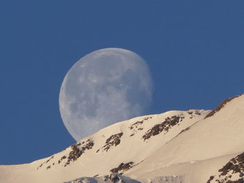 Low angle view of snowcapped mountain against blue sky and moon