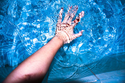 Midsection of person splashing water in swimming pool