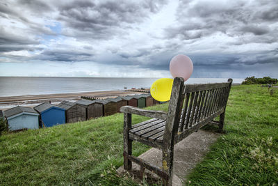 Empty bench at beach against sky