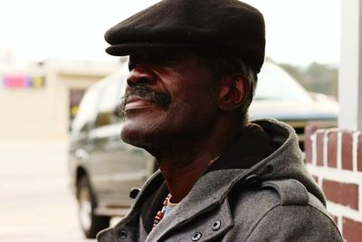 Close-up of thoughtful smiling man wearing flat cap in city