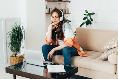 Redhead young modern female freelancer works online in zoom using laptop and headphones.