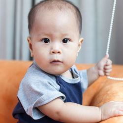 Close-up of toddler holding roller blind chain on sofa at home