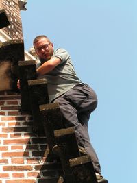 Low angle view of mature man standing on steps against clear sky during sunny day