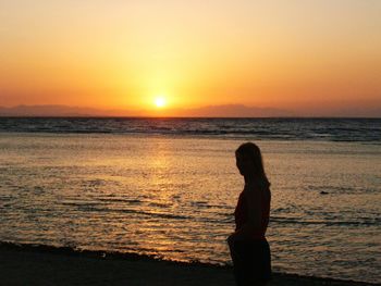 Silhouette woman standing at beach during sunset