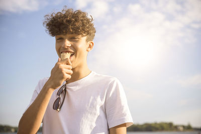 Portrait of happy teenage boy eating ice cream during vacation against sky