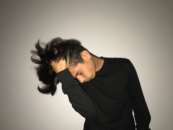 Young man with hand in hair standing against wall