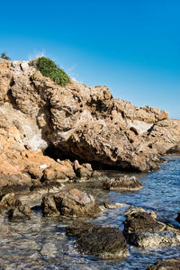 Rock formations in sea against clear blue sky