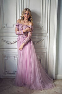 Beautiful young woman in pink lace dress standing at the wall in the white room