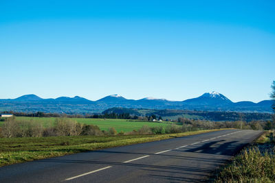 Road leading towards mountains against clear blue sky