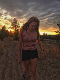 Mid adult woman standing on field against sky during sunset