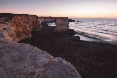 Rocks on beach against sky during sunset