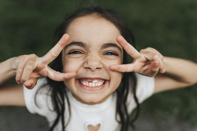 Portrait of happy elementary girl showing peace sign at park