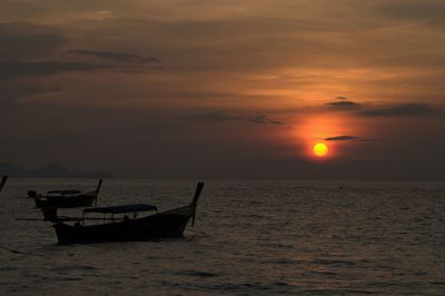 Longtail boats moving on sea against sky during sunset