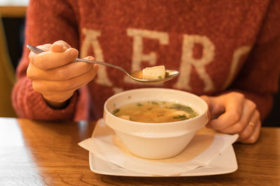 Woman eating fish soup with salmon, sea bass and herbs at seafood cafe. female hand holds full spoon