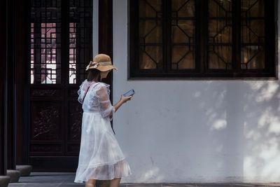 Young woman using smart phone standing by building