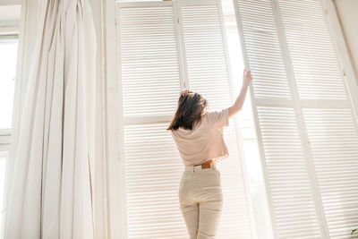 Rear view of woman standing by window at home