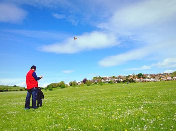 Father and son flying kite on grassy field against sky