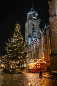 Illuminated christmas tree by building against sky at night