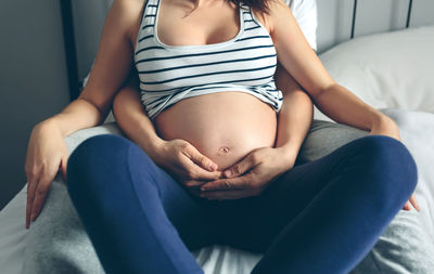 Midsection of woman sitting on bed at home