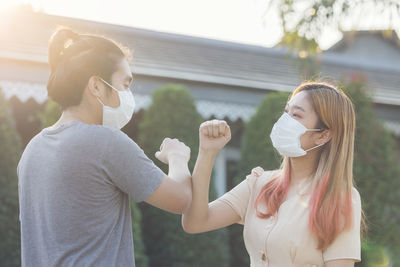 Young asia couple wearing face mask outdoors say hello with elbows outdoors. no hugs, no kisses, 